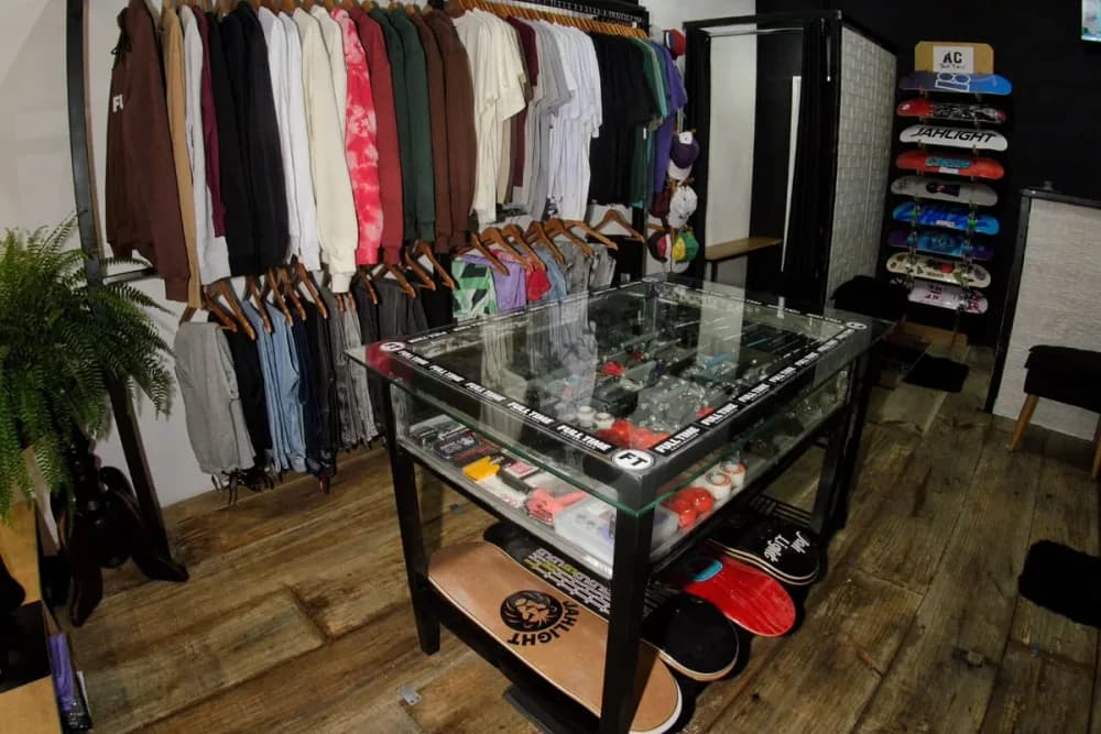 Dentro da Full Time: as araras de camisetas e moletons, a vitrine de vidro e os shapes embaixo